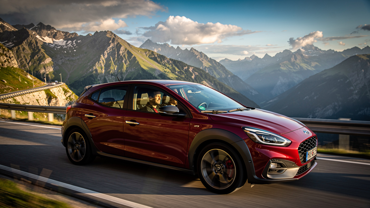 Voiture compacte sportive rouge et grise sur une route sinueuse en montagne, vues extérieure et intérieure dans une ambiance de guide d’achat, lumière dorée et reflets réalistes.